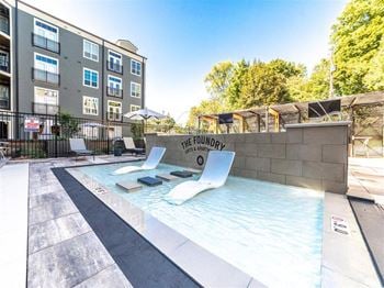 a pool with two lounge chairs in front of an apartment building at The Foundry, South Bend, IN 46617